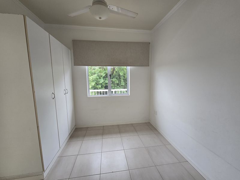 A bright, empty bedroom featuring neutral tiled flooring, built-in cupboards, and a ceiling fan, offering a clean canvas for personalization.