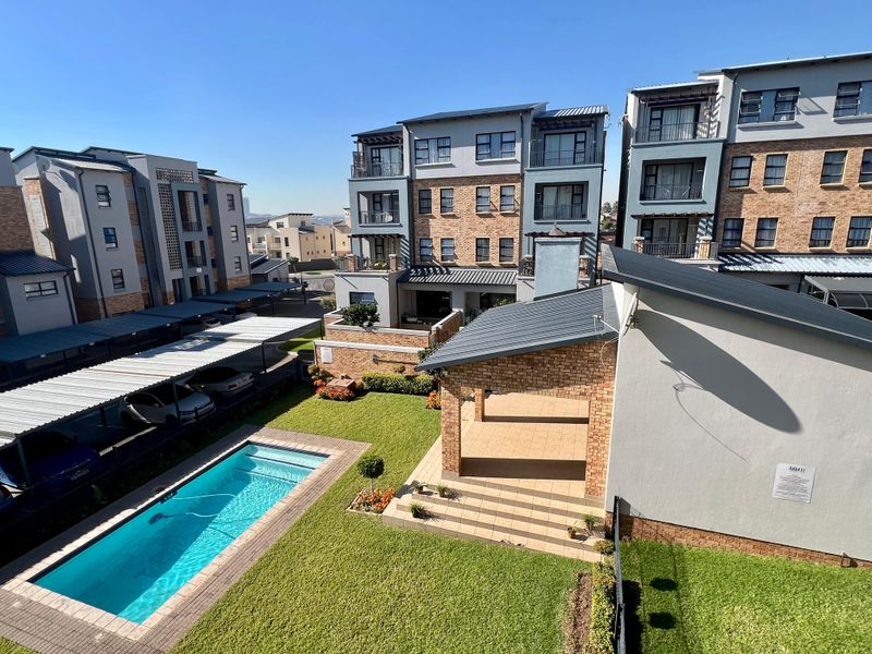 Aerial view of an apartment complex featuring a swimming pool, covered patio area, landscaped garden, and dedicated carport parking facilities.