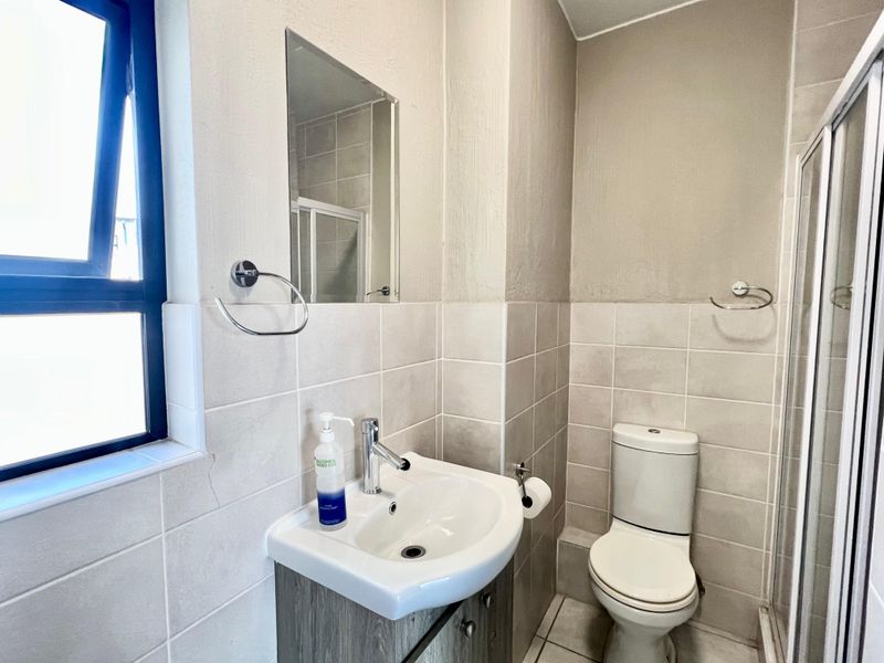 A functional bathroom featuring a vanity basin, toilet, and shower enclosure with neutral wall tiling and natural light from the window.