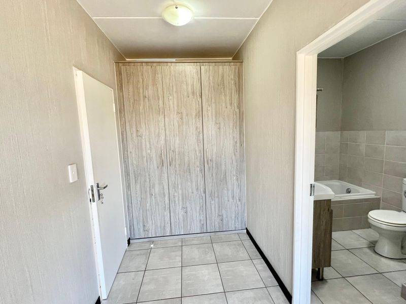 A clean, functional hallway featuring built-in wood-grain cupboards and neutral tiled flooring, providing direct access to an adjacent bathroom.