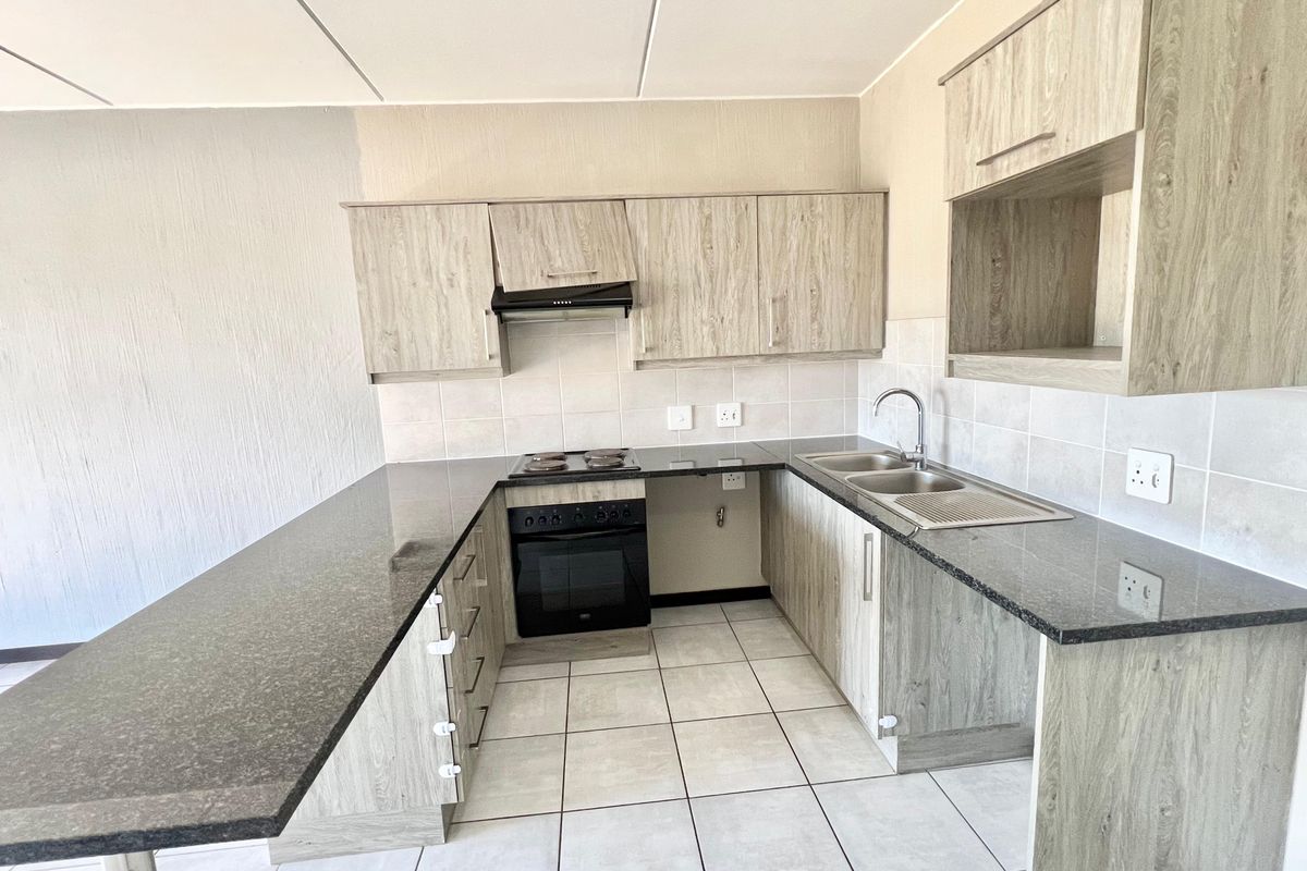 A functional kitchen featuring laminate cabinetry, granite countertops, a built-in oven with hob, and a stainless steel double sink with tiled backsplash.