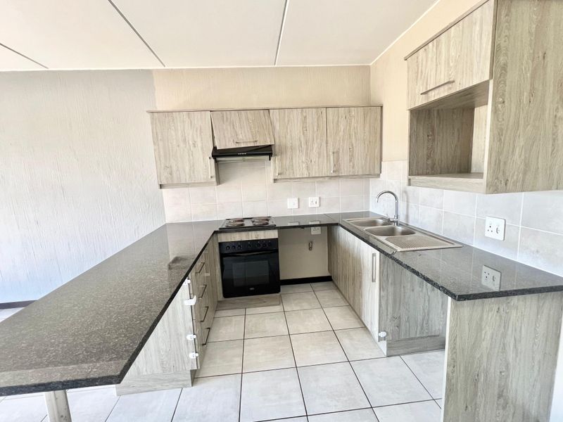 A functional kitchen featuring laminate cabinetry, granite countertops, a built-in oven with hob, and a stainless steel double sink with tiled backsplash.