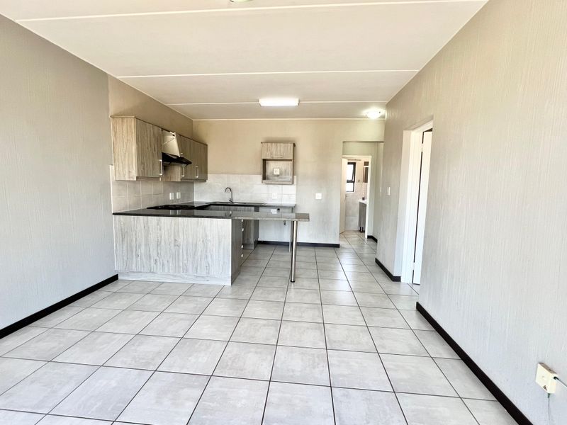 An open-plan kitchen area featuring modern wood-look cabinetry, tiled flooring, and a breakfast counter, offering a clean and functional space.
