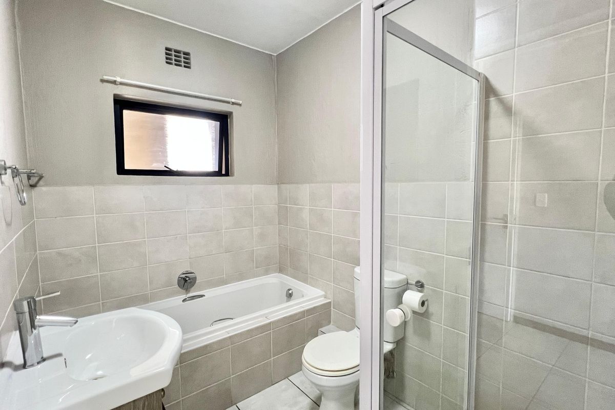 A clean, functional bathroom featuring a built-in bathtub, separate shower enclosure, pedestal basin, and neutral ceramic tiling throughout.