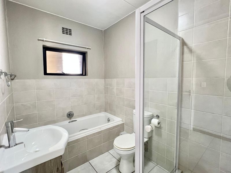 A clean, functional bathroom featuring a built-in bathtub, separate shower enclosure, pedestal basin, and neutral ceramic tiling throughout.