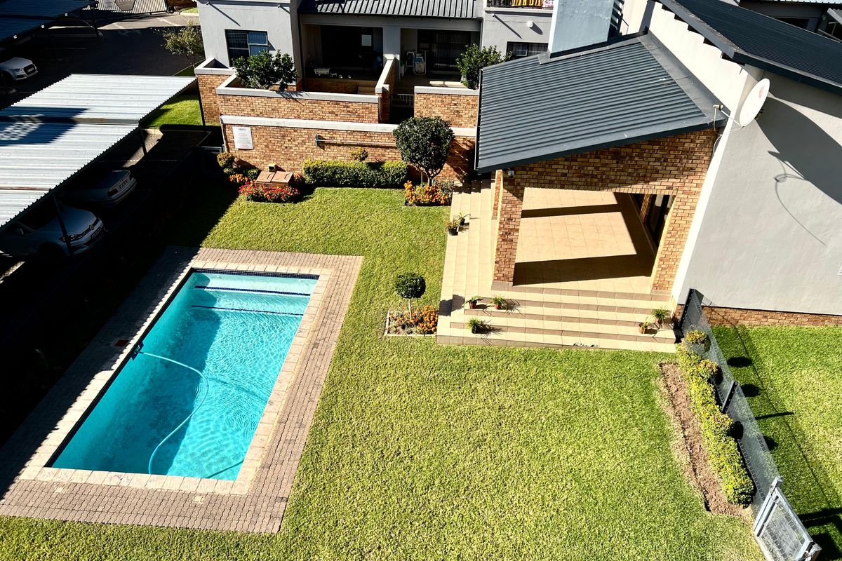 Aerial view of an apartment complex featuring a private swimming pool, covered patio, landscaped garden, and dedicated carport parking.