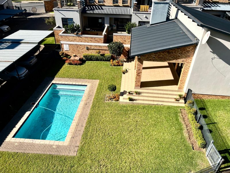 Aerial view of an apartment complex featuring a private swimming pool, covered patio, landscaped garden, and dedicated carport parking.