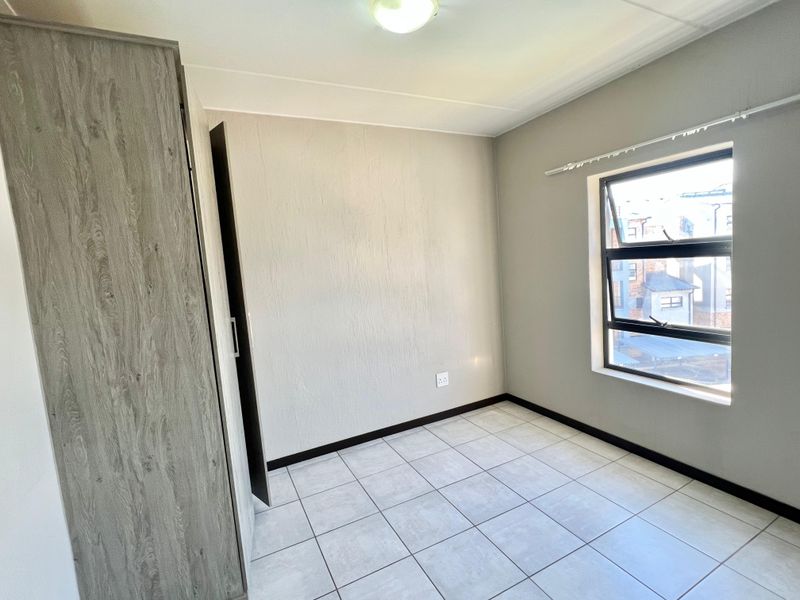A clean, empty bedroom featuring neutral tiled flooring, a built-in wardrobe, and an aluminium-framed window providing natural light.