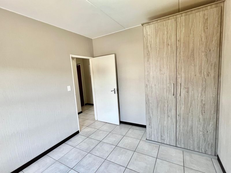 A clean, empty bedroom featuring neutral wall tones, light-colored tiled flooring, and a modern built-in wardrobe with wood-grain finish.