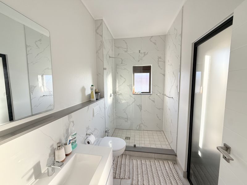 Modern bathroom featuring a walk-in shower with marble-look wall tiles, a sleek vanity with basin, and a contemporary frosted glass door.