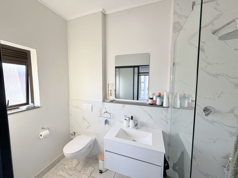 Modern bathroom featuring a wall-mounted toilet, sleek vanity with integrated sink, and a spacious glass-enclosed shower with marble-look tiling.