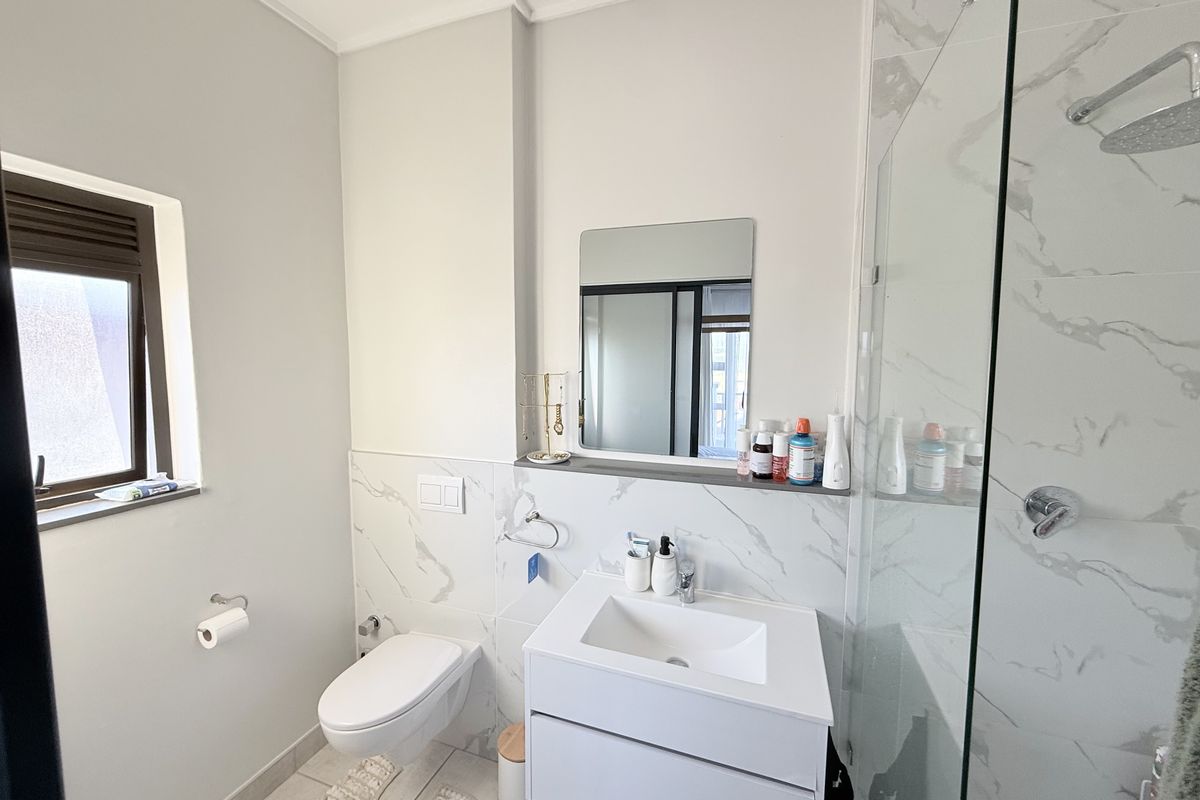 Modern bathroom featuring a wall-mounted toilet, sleek vanity with integrated sink, and a spacious glass-enclosed shower with marble-look tiling.