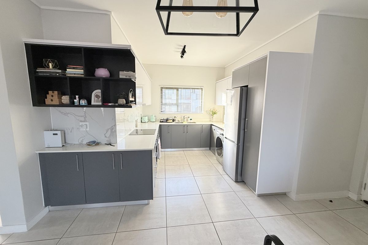 Modern kitchen featuring sleek grey and white cabinetry, stone countertops, integrated appliances, and large format floor tiles in an open-plan layout.