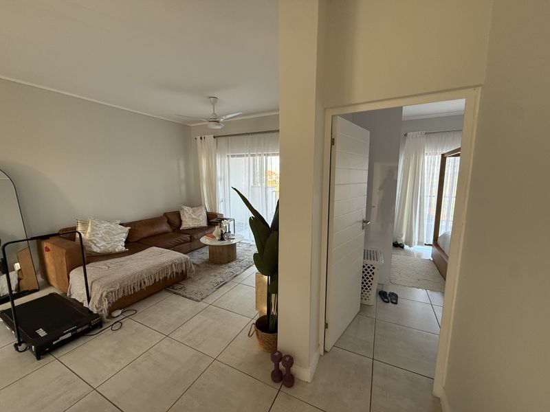 A bright living area featuring neutral tiled flooring, a ceiling fan, and direct access to a balcony through sliding glass doors.