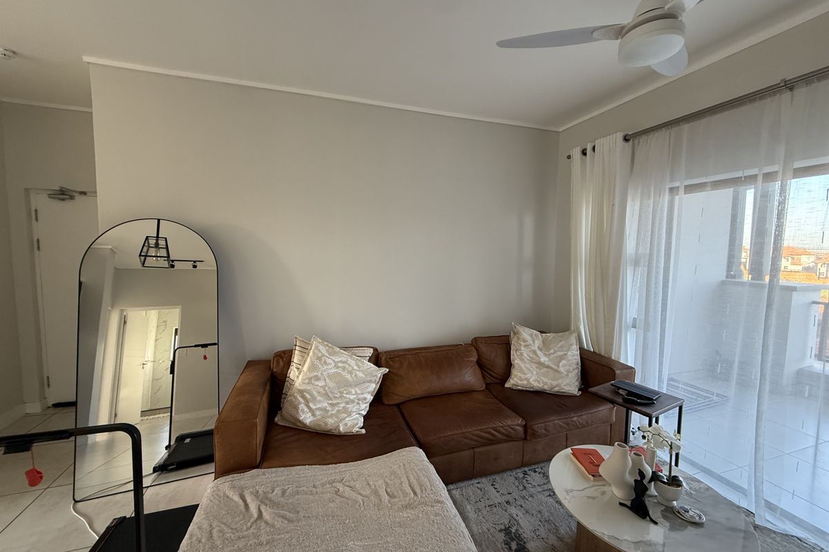 A bright living room featuring tiled flooring, a ceiling fan, and large sliding glass doors providing access to an outdoor balcony area.