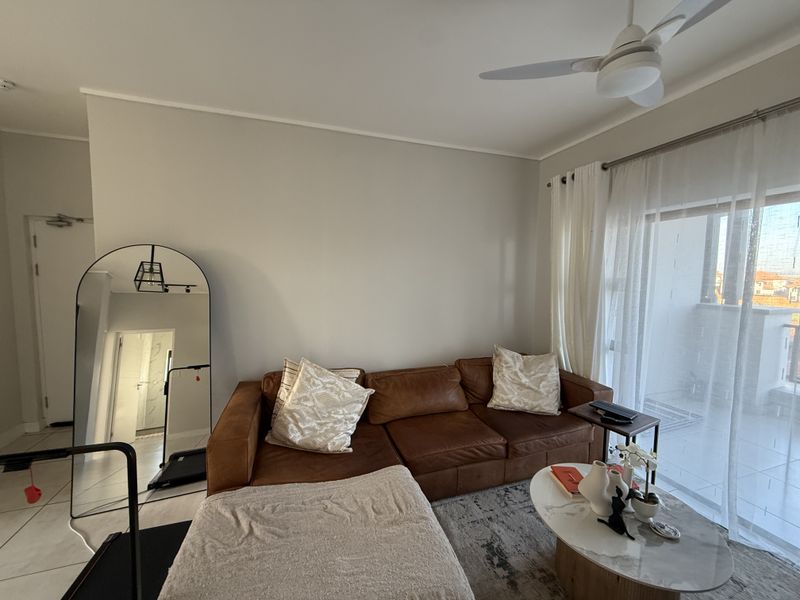 A bright living room featuring tiled flooring, a ceiling fan, and large sliding glass doors providing access to an outdoor balcony area.
