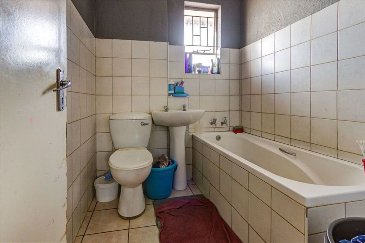 A compact bathroom featuring a pedestal basin, built-in bathtub, and toilet, finished with ceramic wall and floor tiles.