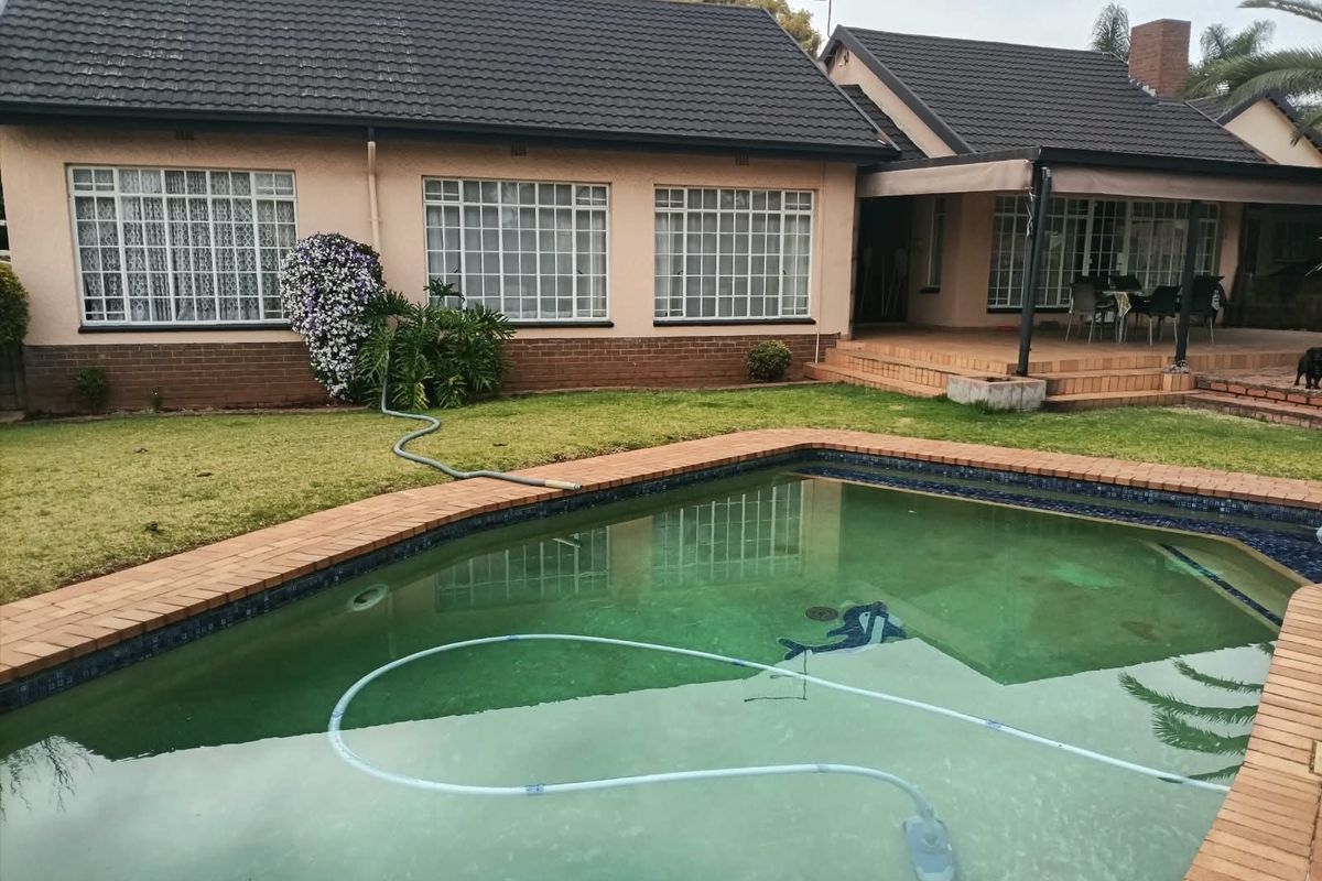 Rear view of the house featuring a swimming pool, covered patio area, and established garden with brick and tile exterior finishes.