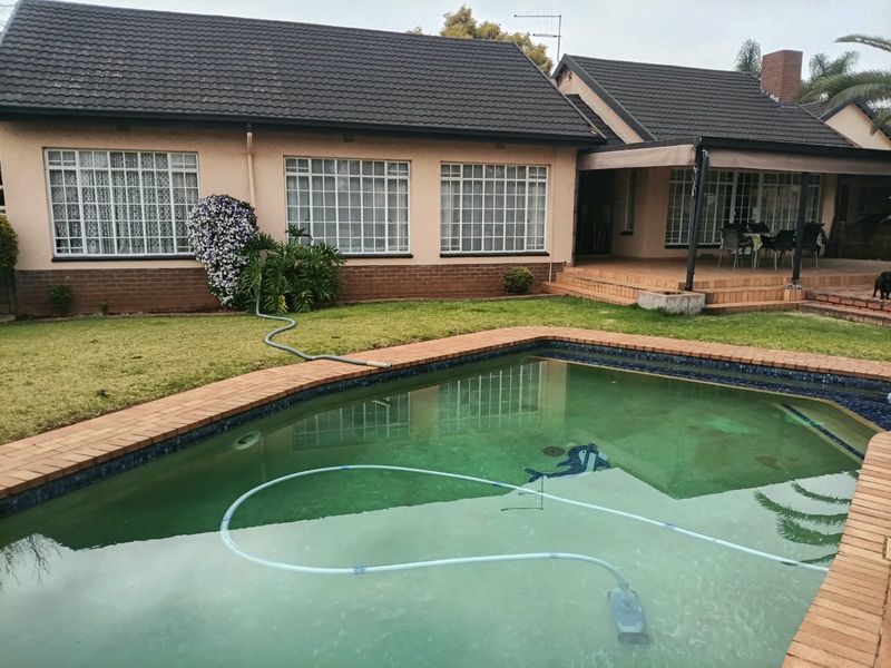 Rear view of the house featuring a swimming pool, covered patio area, and established garden with brick and tile exterior finishes.