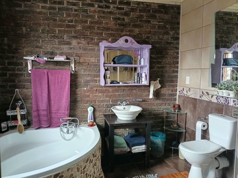 Bathroom featuring a corner bathtub, vessel sink vanity, and toilet, accented by an exposed brick feature wall and tiled finishes.