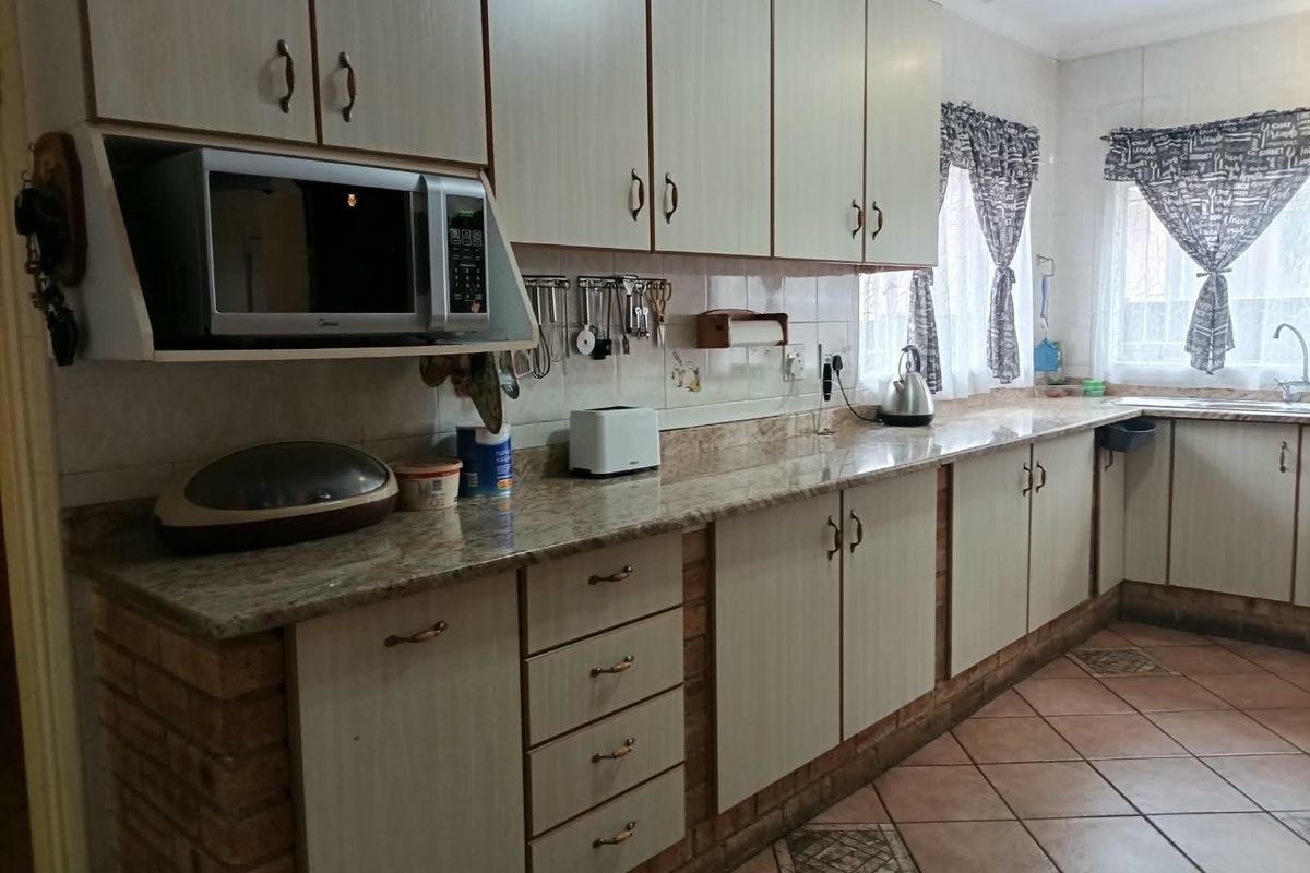 A functional kitchen featuring laminate cabinetry, granite countertops, brick base detailing, and tiled flooring with a built-in microwave and stainless steel sink.