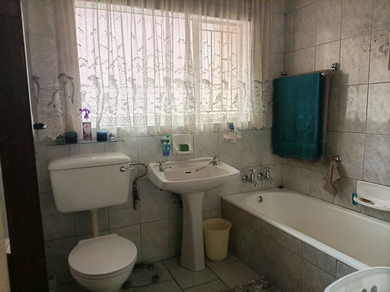 A functional bathroom featuring a pedestal basin, toilet, and bathtub with full-height wall tiling.