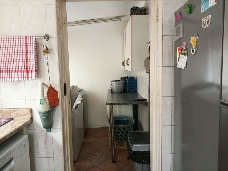 A functional scullery area featuring tiled walls, laminate countertops, and wall-mounted cabinetry, providing additional utility and storage space adjacent to the main kitchen.