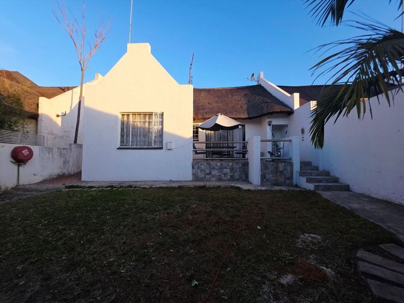 Rear view of a cluster home featuring a thatched roof, a raised patio area with stone cladding, and a private garden space.