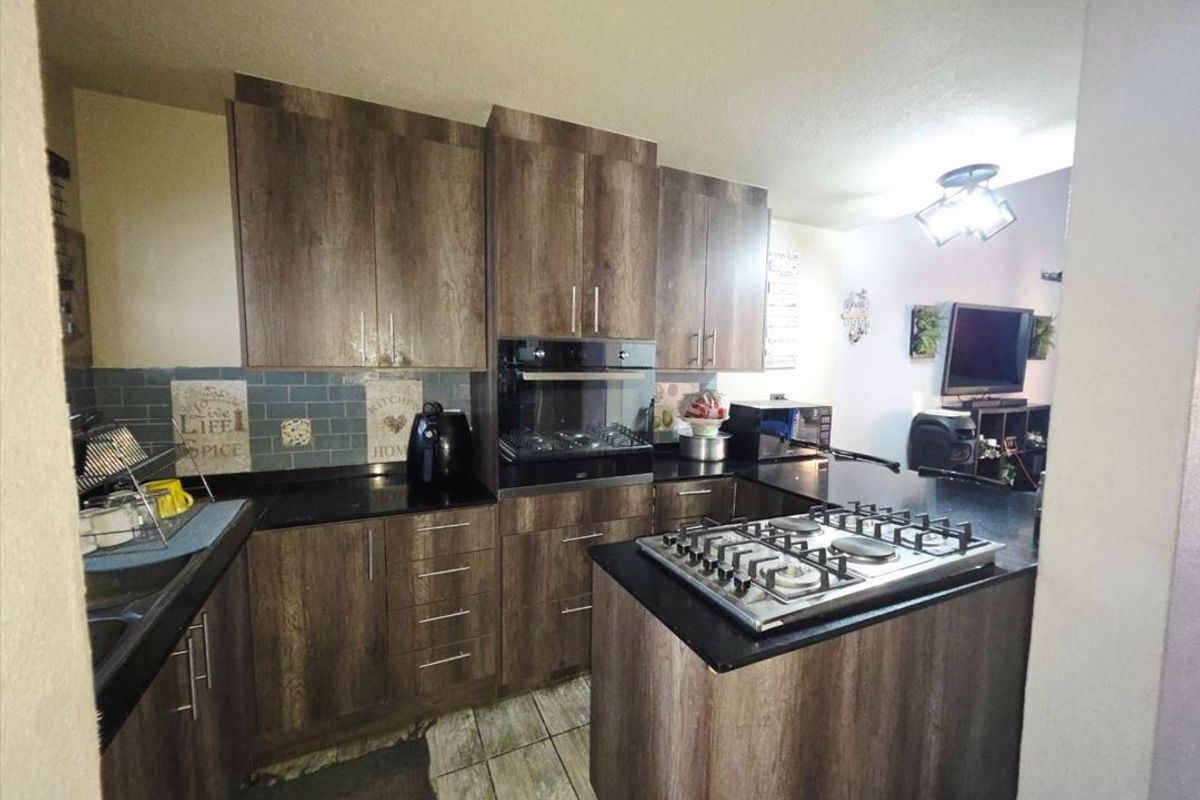 A functional kitchen featuring wood-look cabinetry, granite countertops, a built-in oven, and a gas hob, with an adjacent open-plan living area.