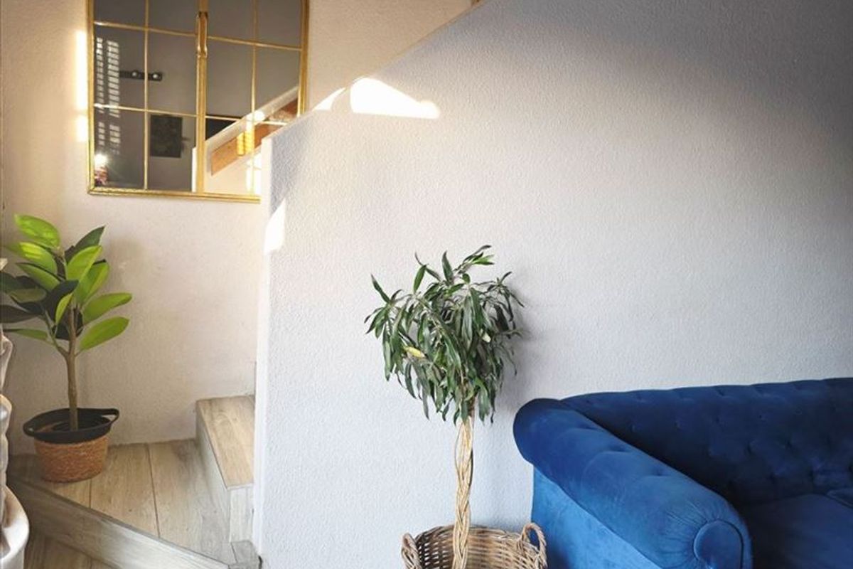 A living area featuring tiled flooring and a staircase leading to an upper level, accented by a decorative arched wall mirror.