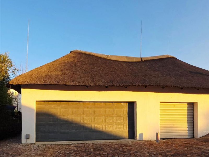 Exterior view of a detached garage featuring a traditional thatch roof, double and single garage doors, and a paved driveway.