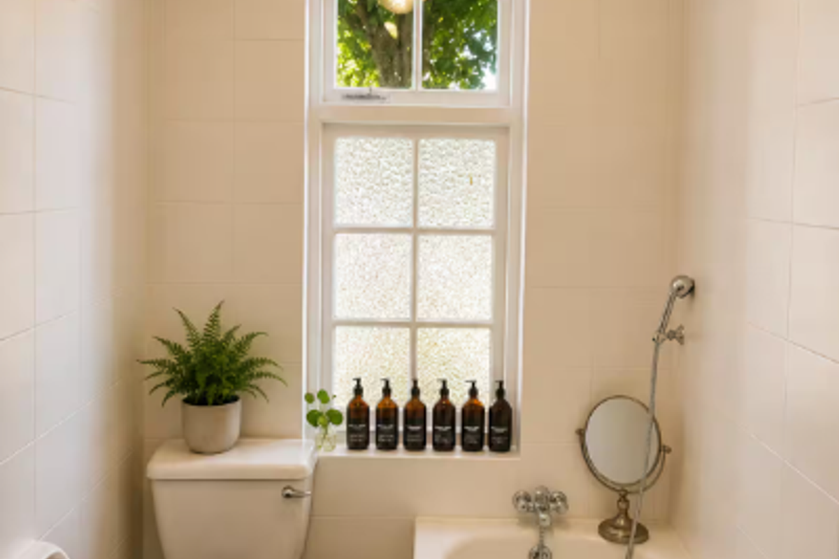 A clean, well-maintained bathroom featuring a white bathtub with handheld shower mixer, a standard toilet, and full-height wall tiling.