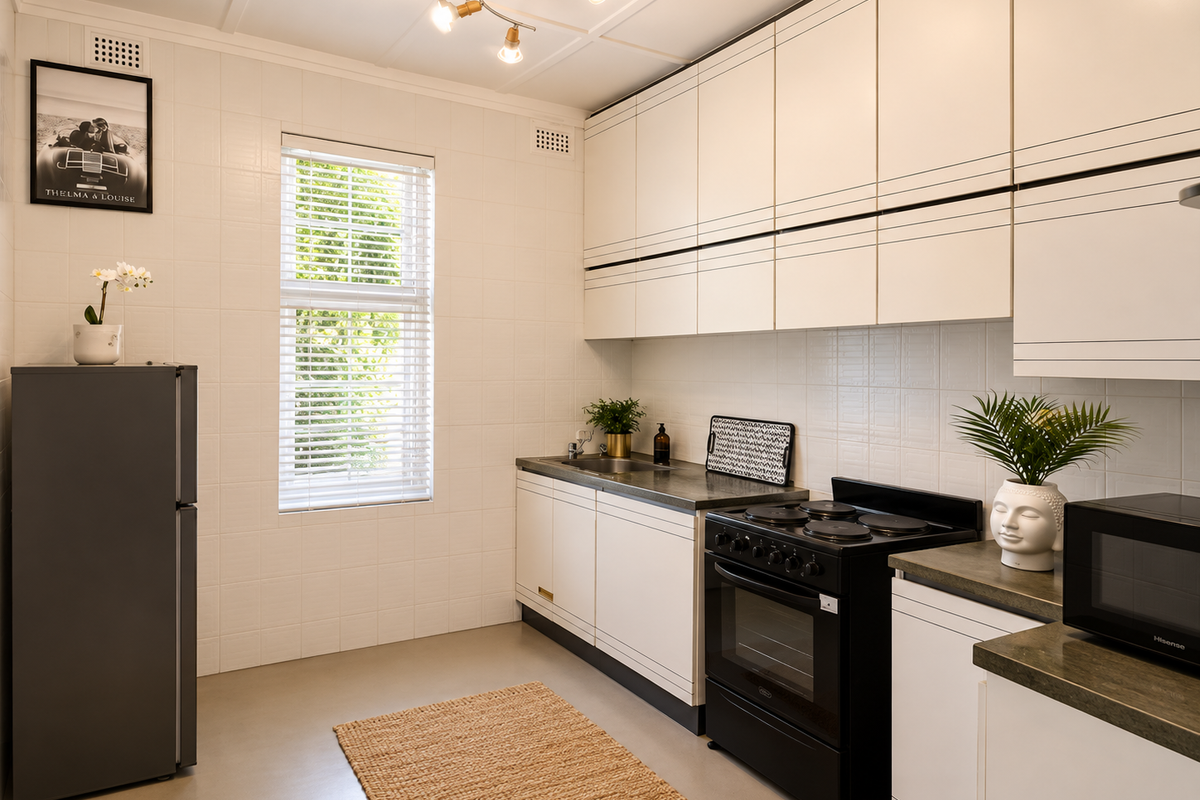 A clean, functional kitchen featuring white cabinetry, dark countertops, a black electric stove, and a window with venetian blinds.