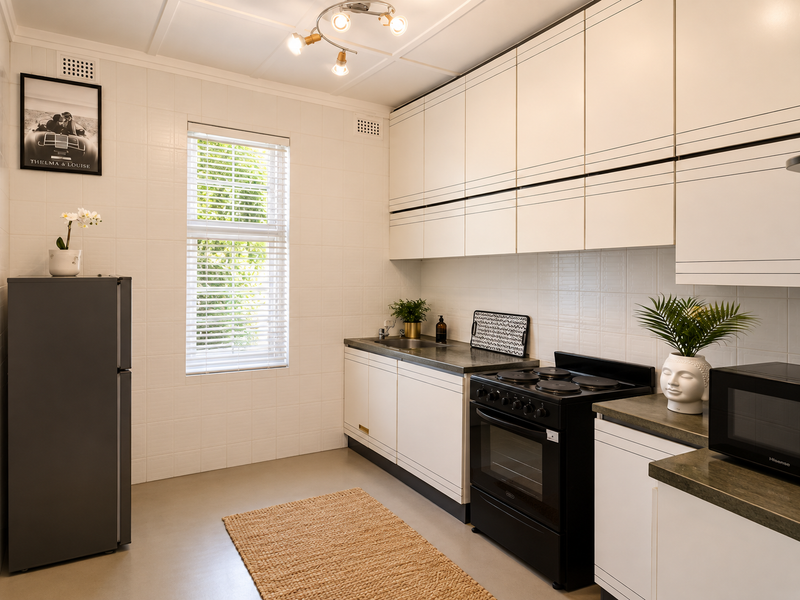 A clean, functional kitchen featuring white cabinetry, dark countertops, a black electric stove, and a window with venetian blinds.