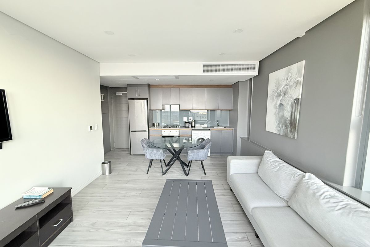 Modern open-plan living area featuring a sleek kitchen with built-in cabinetry, gas hob, and integrated appliances, complemented by neutral tones and recessed lighting.