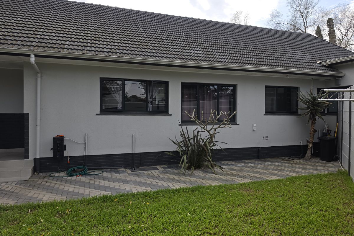 Rear view of the apartment featuring a paved patio area, well-maintained lawn, and modern dark-framed windows under a tiled roof.