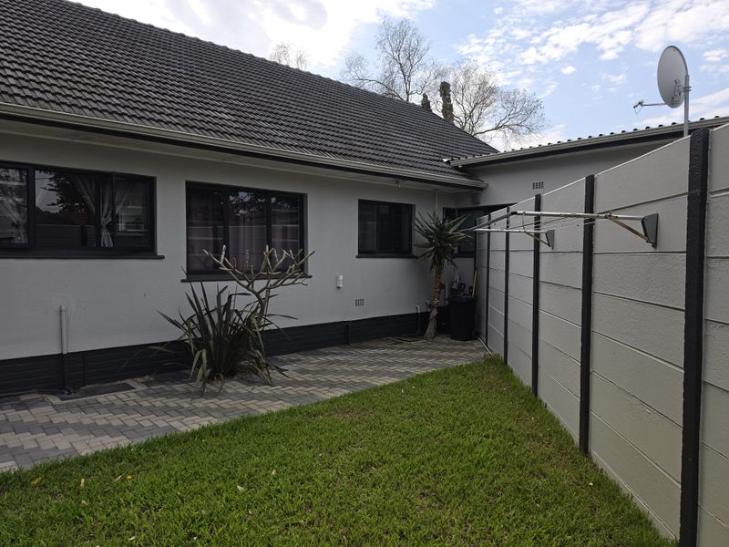 Rear exterior view featuring a paved patio area, a well-maintained lawn, and a secure precast concrete boundary wall with a mounted clothesline.