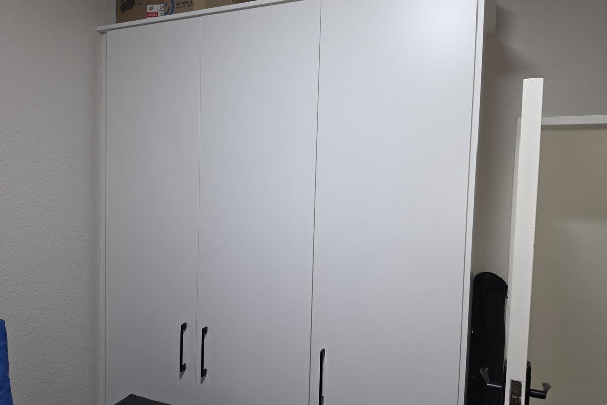 A bedroom featuring a modern, white built-in wardrobe with sleek black handles, providing ample storage space.