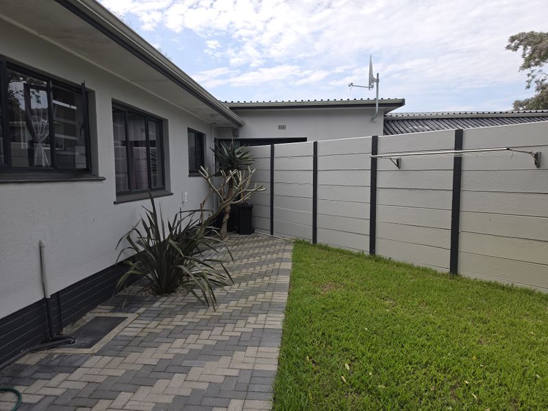 A well-maintained rear exterior area featuring a paved walkway, a small lawn, and a secure precast concrete boundary wall with a mounted clothesline.