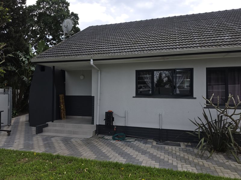 A well-maintained rear exterior view of the apartment featuring a paved patio area, modern dark-framed windows, and a tiled roof.