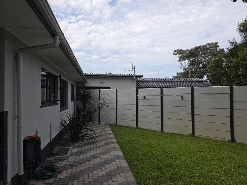 A well-maintained rear exterior area featuring a paved walkway, a neat lawn, and a secure precast concrete boundary wall with an integrated clothesline.