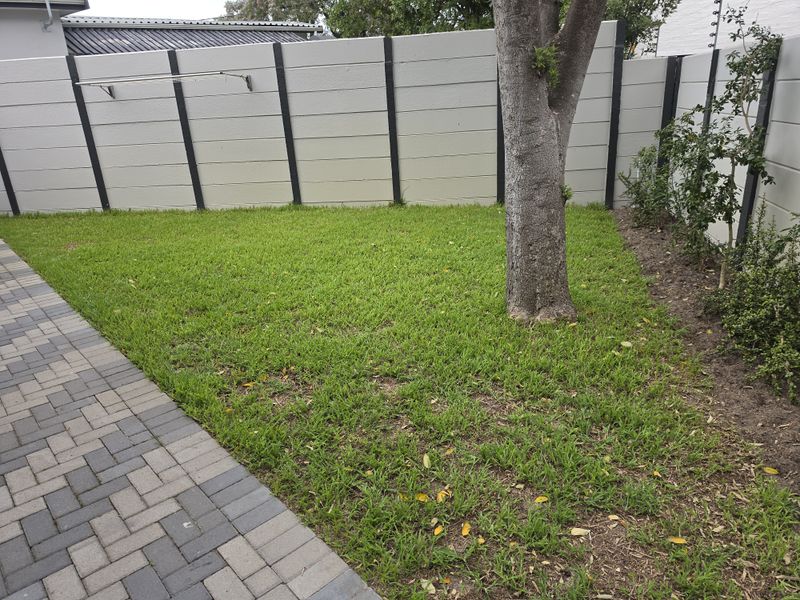 A private rear garden featuring a paved walkway, a well-maintained lawn, and a secure precast concrete boundary wall with a wall-mounted clothesline.