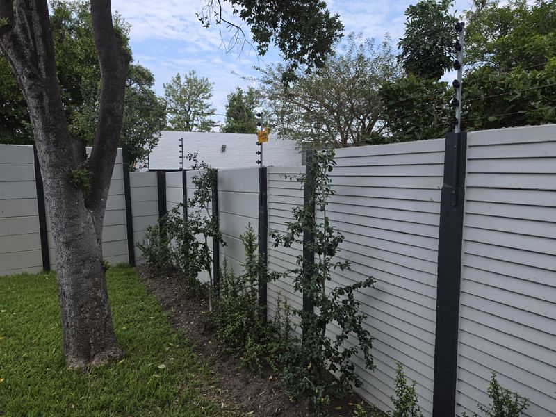 A well-maintained rear garden area featuring a secure precast concrete boundary wall equipped with electric fencing.