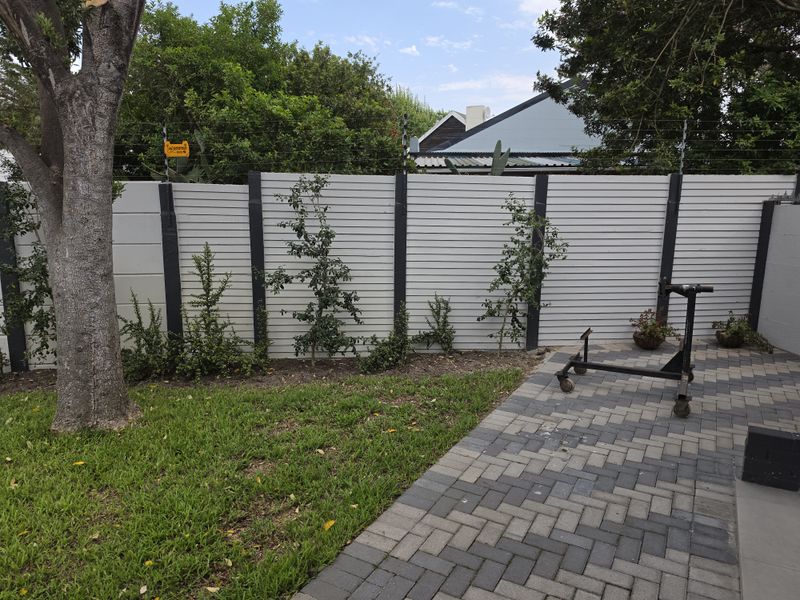 A well-maintained rear garden area featuring a paved patio, lawn, and secure boundary wall with integrated electric fencing.