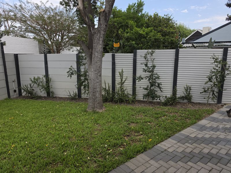 A well-maintained rear garden area featuring a modern horizontal slat fence with integrated electric security fencing and a paved walkway.