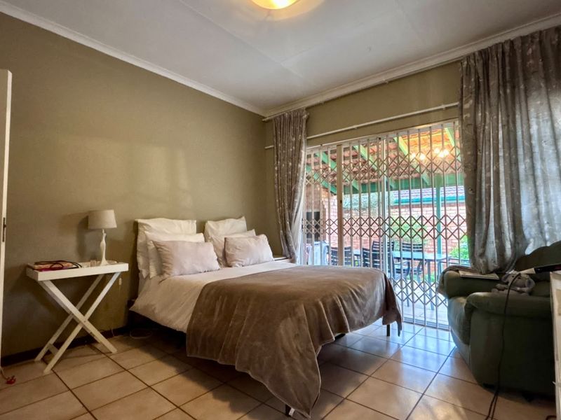 A bedroom featuring tiled flooring and a sliding glass door with a security gate, providing direct access to an outdoor patio area.