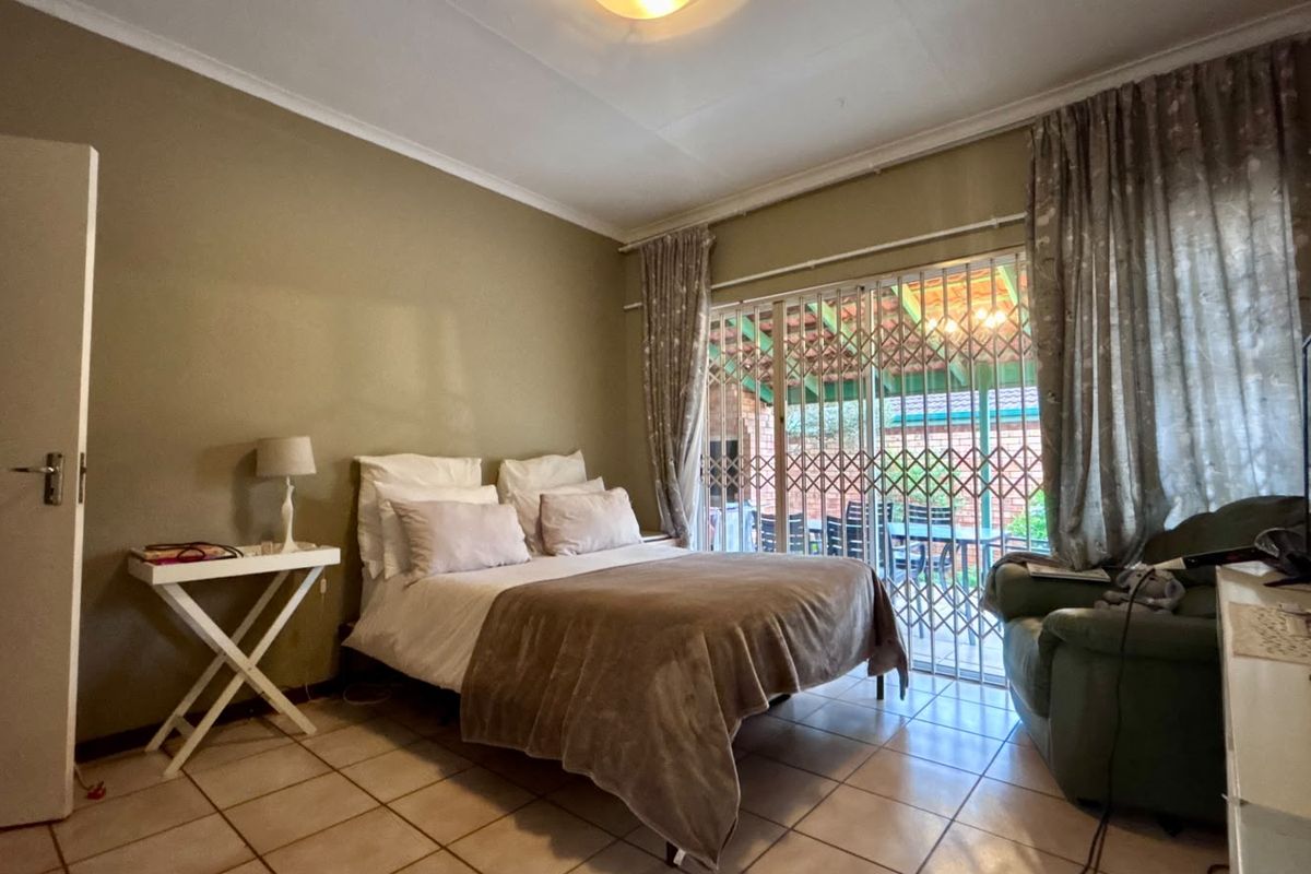 A bedroom featuring tiled flooring and a sliding glass door with a security gate, providing direct access to an outdoor patio area.