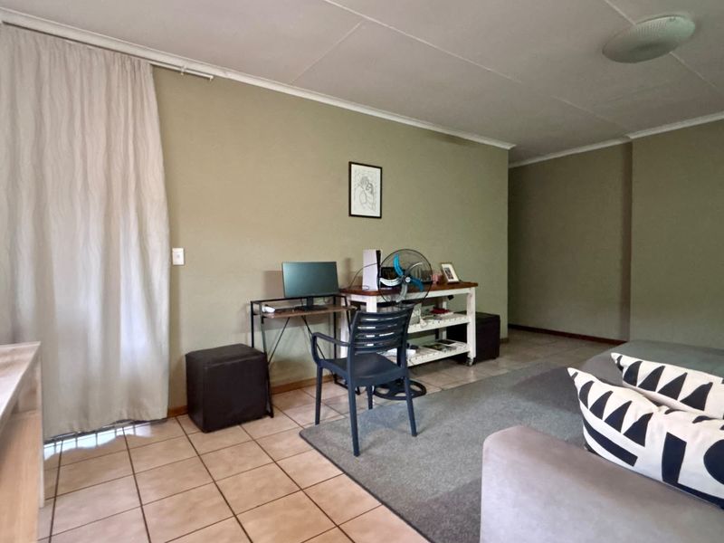 A living area featuring neutral wall tones and tiled flooring, offering a versatile space for relaxation or a home office setup.