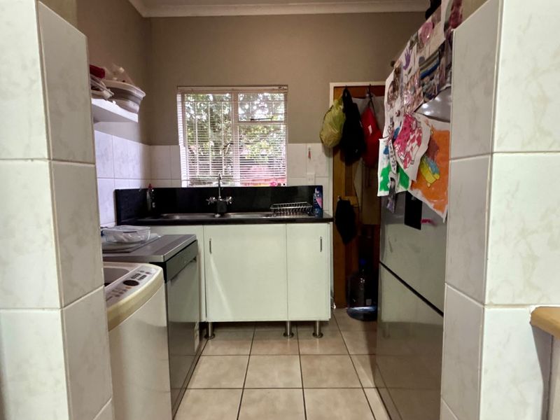 A functional scullery area featuring tiled flooring, built-in cabinetry, and a double sink with a window providing natural light.