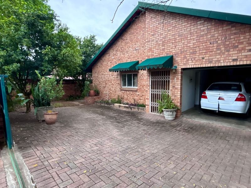 Front exterior view featuring a brick facade, paved driveway, and integrated garage with security gate and window awnings.
